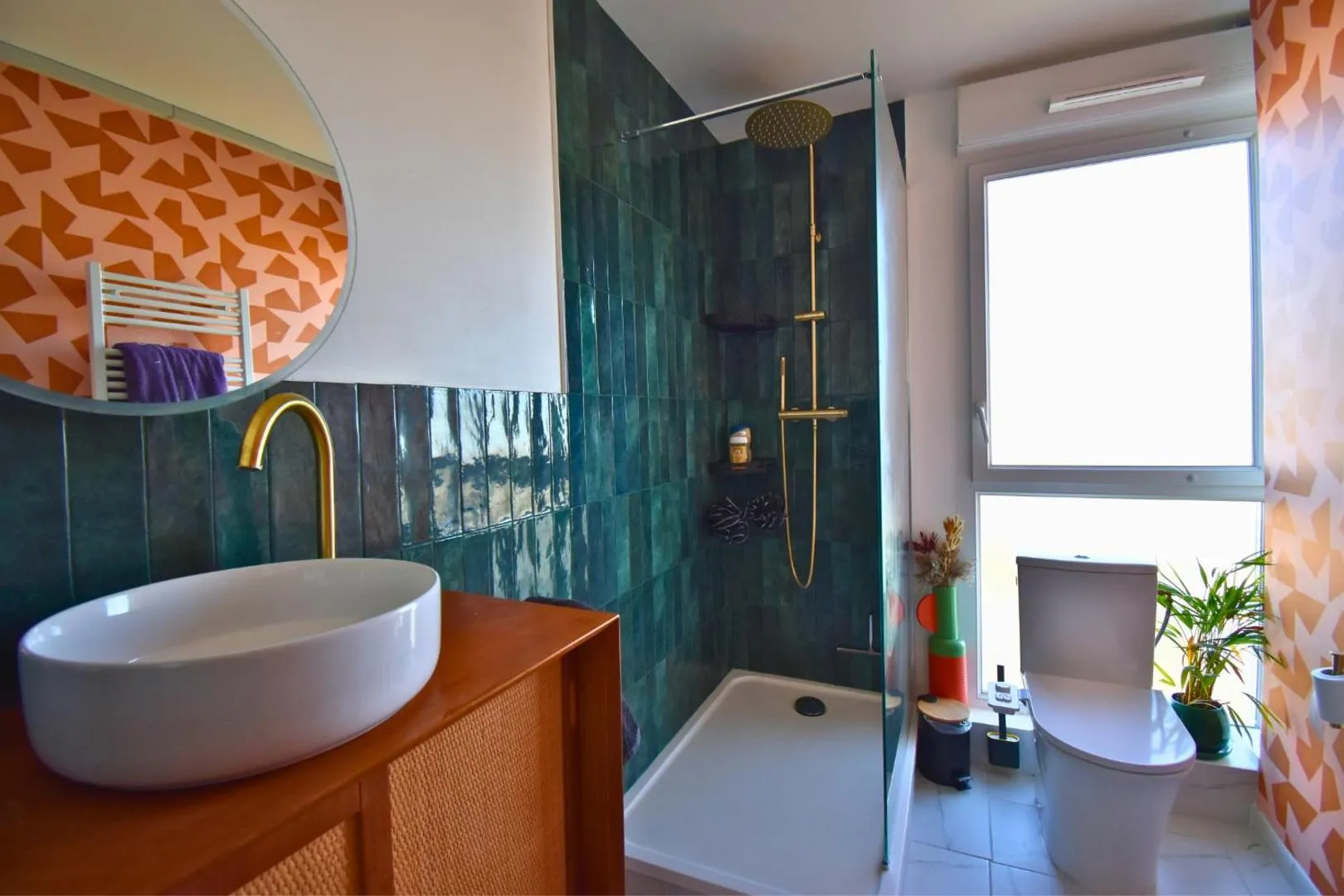 Salle de bain après : zellige vert profond, robinetterie dorée, meuble cannage orange, papier peint géométrique orange, miroir rond, douche à l'italienne