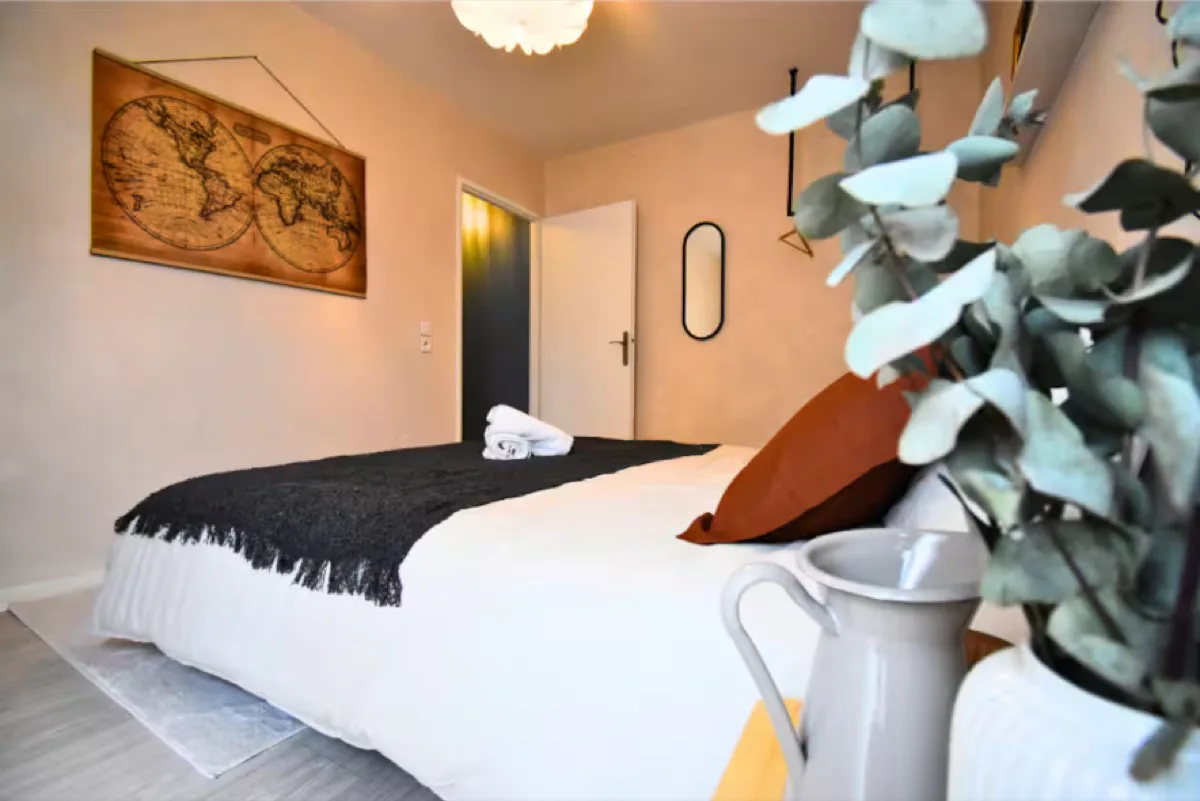 Chambre après home staging : literie blanche et gris, coussins terracotta, tableau carte du monde, plante, éclairage doux