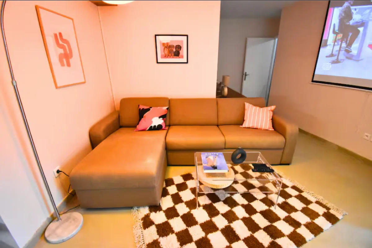 Séjour après : canapé en L caramel, tapis damier marron/crème, tableau orange, ambiance vintage