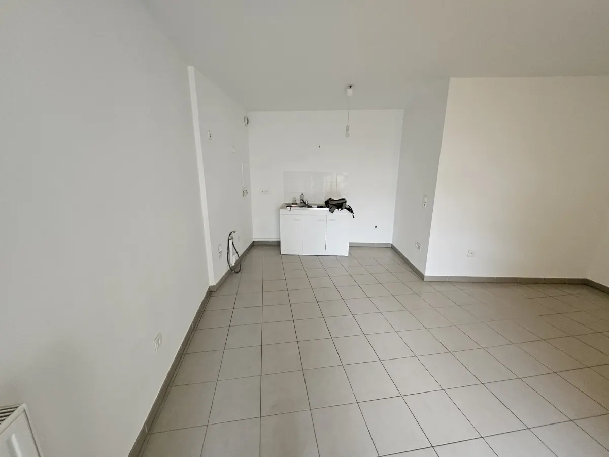 Séjour de location courte durée avant home staging, vide, avec murs blancs, carrelage gris et kitchenette