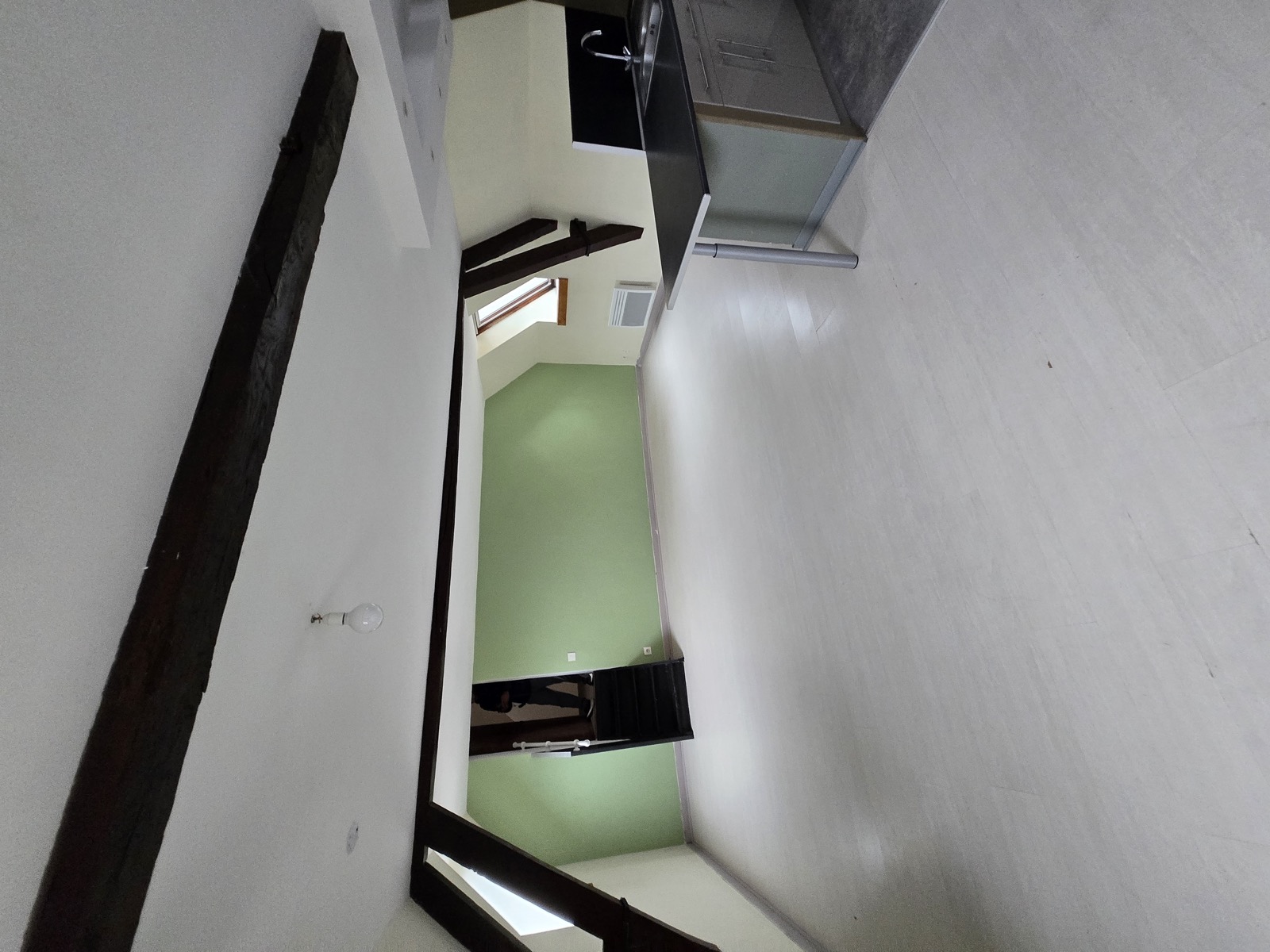 Le Loft des Charpentiers vide : espace ouvert sous charpente, poutres noires, îlot cuisine brut