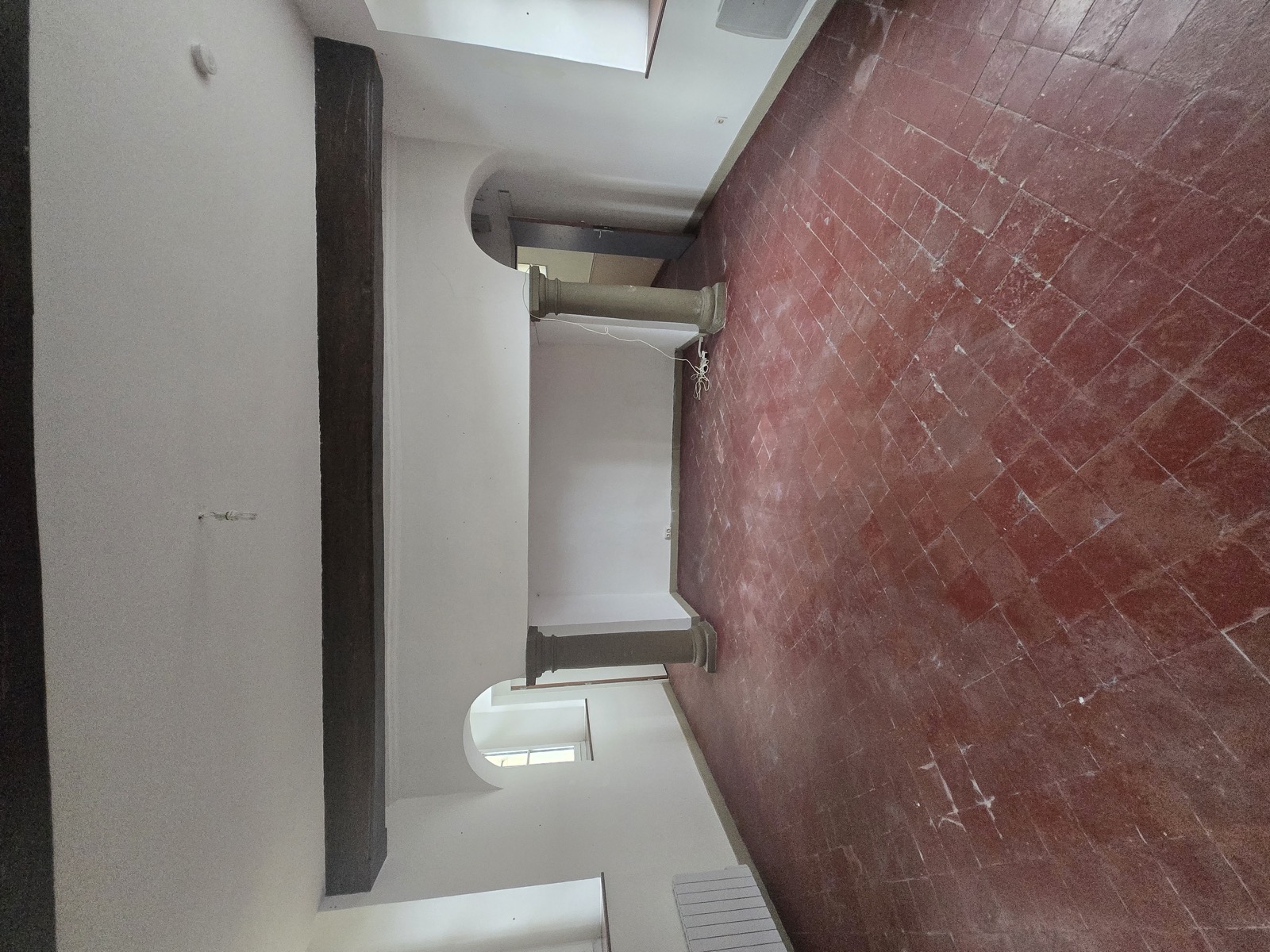 La Salle des Arches vide : colonnes en pierre, arches, carrelage terracotta, murs nus